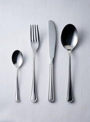 Four pieces of silverware/ cutlery on white cotton table cloth, ready to be used, including spoon,...
