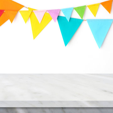 Colorful party flags hanging on white wall and white marble table background, birthday, anniversary, celebrate event, festival greeting card background