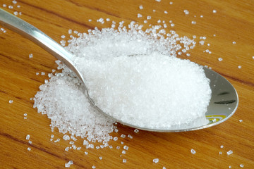White sugar on steel spoon wood table background. The taste sweet sugar.