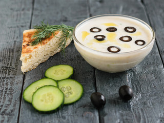 Tzatziki sauce in a glass bowl and olives on a dark wooden table with a piece of bread.