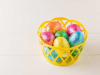 Yellow basket with colorful eggs on a wooden table.