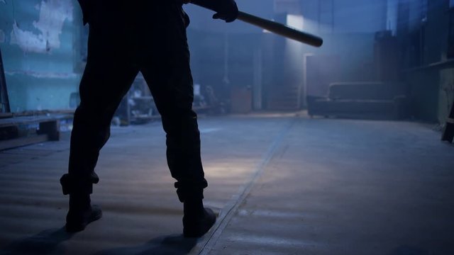 Masked man with baseball bat walking in abandoned place. Shot on RED Cinema Camera in slow motion.