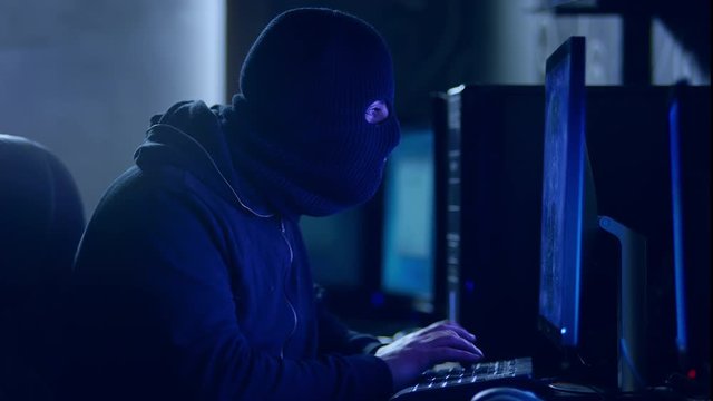 Hacker with mask breaking code. . Hacker with mask using laptop and computers to crack the internet from hackers dark room. Shot on RED Cinema Camera.