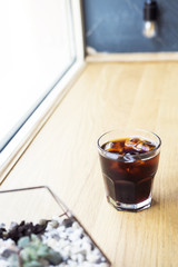 Cold brew coffee with ice cubes on the window wooden bar. Urban coffee shop.