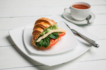 Croissant with cheese, tomatoes and leaves of spinach on a white plate. Vegan breakfast.