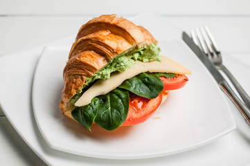Croissant with cheese, tomatoes and leaves of spinach on a white plate. Vegan breakfast.