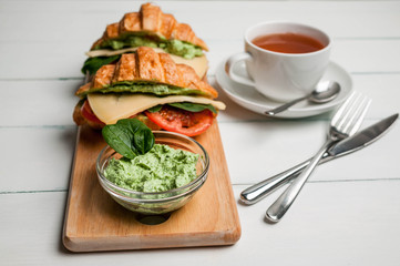 Croissant with cheese, tomatoes, leaves of spinach and green cream cheese on a light background. Vegan breakfast.