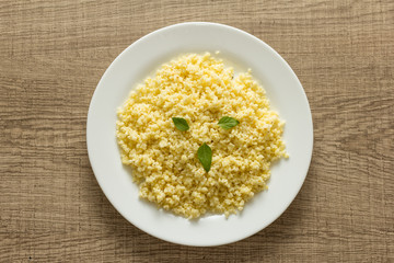 Cooked Millet cereal grain on white plate and wooden table. Overhead, flat lay of meal.