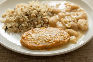 Pork chop, Brown rice and white beans. White dish on wooden table. Detail of food dish, closeup, selective focus.