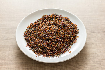 Cooked Red and Black Quinoa mixed. Meal on white dish and wooden table.