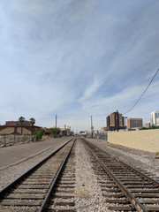 Fototapeta na wymiar Double parallel steel rail tracks laid on wooden sleepers of old but still running railroad crossing downtown of Phoenix in Arizona