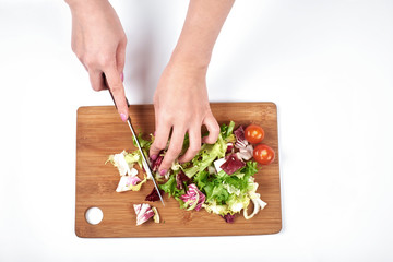 Closeup of woman hands slicing salad and vegetables on a wooden board, isolated on white background