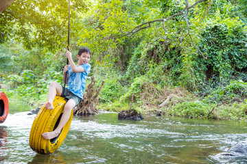 Young asian boy smiling while palying swing chair in the river