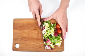 Closeup of woman cook's hands slicing salad and vegetables on a wooden board, isolated on white background, copy space