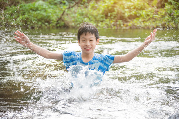 Young asian boy smiling while palying splash water in the river