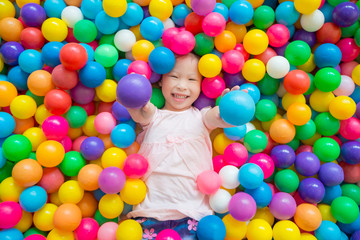 Fototapeta na wymiar Little asian girl smiling while lying on many color ball at indoors playground