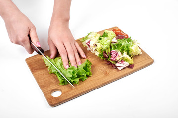 Closeup of woman hands slicing salad and vegetables on a wooden board, isolated on white background