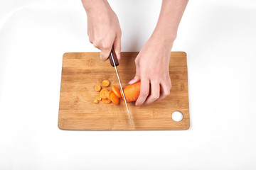 Closeup of woman cook's hands, slicing the carrot on a wooden board, isolated on white background