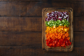 Chopped fresh vegetables arranged on cutting board on dark wooden table with copy space, top view