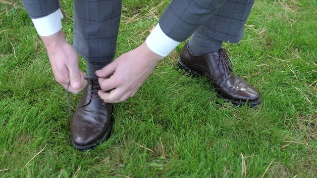 Man tying patent leather shoes on the grass.
