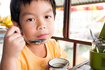 A hungry boy is sitting at the wooden table for eat dessert at restaurant with orange t-shirt