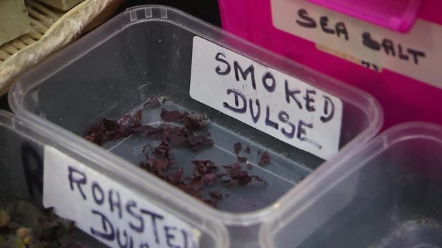 Close up shot of container of smoked dulse as a hand picks some up. 