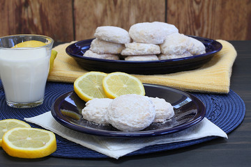 Lemon cookies with powdered sugar with lemons and a glass of milk.