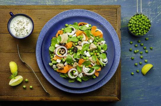 Tuna salad with fresh green peas,carrot,onion,arugula,,black olives,basil and feta cheese placed with garlic yogurt sauce. Top view with close-up