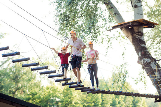A young couple with a child walking on a rope bridge with insurance. The concept of active family rest, spot. Rope park on the tree