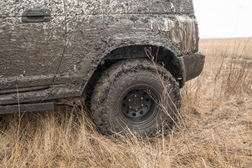 Fototapeta na wymiar The wheels of the car are soiled in mud and equipped for off-road driving stand in a field with dry grass