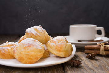 Delicious eclairs sprinkled with icing sugar, stand on a wooden table. Copy spase.