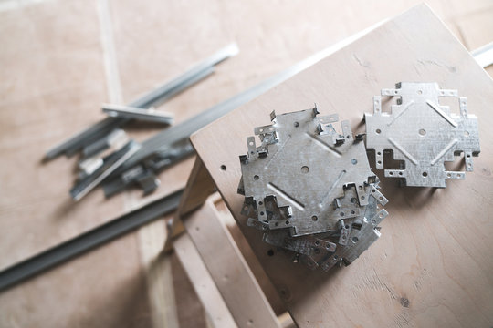 a set of metal connectors called "crab" for working with plasterboard on the ceiling. Metal objects lying on a wooden stepladder for repair of quilt.