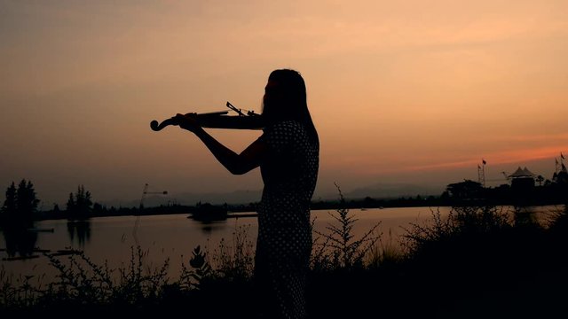 Silhouette woman playing violin with sun set, 