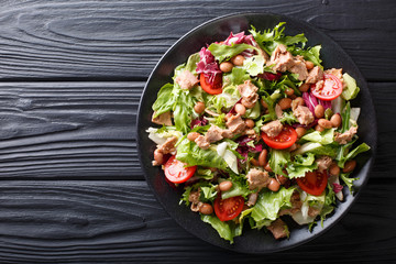 Healthy hearty salad of tuna, borlotti beans, tomatoes, lettuce close-up on a plate. horizontal top view