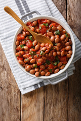 Stewed cranberry beans or borlotti in tomato sauce with herbs close-up in a bowl. Vertical top view from above