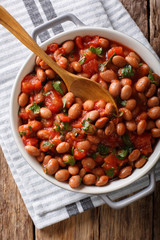 Organic Borlotti beans in tomato sauce with herbs close-up in a bowl. Vertical top view from above