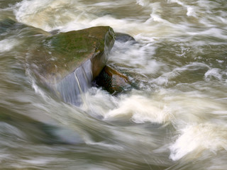 Long exposure of fast moving water over boulders on a river bed.