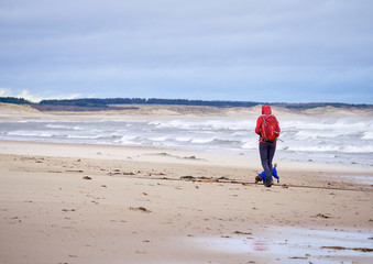 A hiker and their dog walking on the beach of Druridge Bay, Northumberland in England UK.
