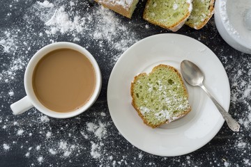 Mint cake sprinkled with powdered sugar on dark surface with cup of coffee