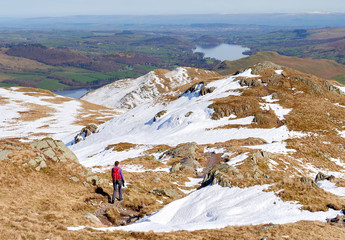 A female hiker descending from a snow covered Place Fell and the Knight summit in the English Lake District.