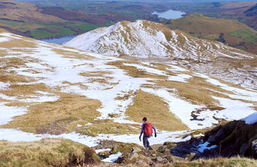 A female hiker descending from a snow covered Place Fell and the Knight summit in the English Lake...