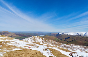 A female hiker descending from a snow covered Place Fell summit in the English Lake District.
