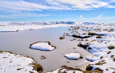 A tarn below Place Fell with the snow covered mountains of Martindale Common in the Lake District, England, UK.