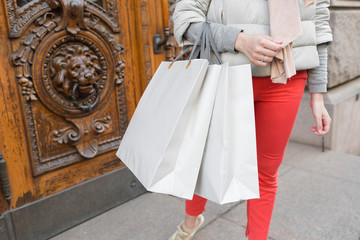 Shopaholic beautiful happy woman goes shopping in the city. Young girl in red pants and a lot of grey paper bags her hands. The concept of shopping, sales and purchases of things.