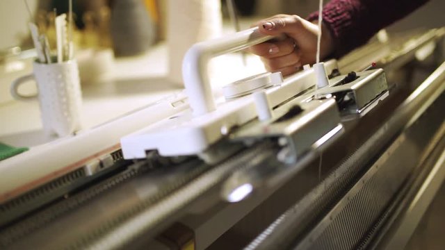 Manual worker making knitted texture on weaving machine at textile factory. Close up female hands working on knitting machine. Manufacturing weaving fabric on loom machine