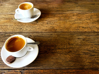 Two cups of strong black coffee stand side by side on a wooden table in a cafe.