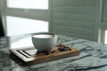 Closeup image of a cup of hot coffee and a wooden saucer on the table in cafe
