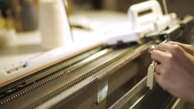 Worker hands making knitted fabric on weaving machine at textile factory. Industrial equipment. Close up woman using loom machine for work in sewing workshop. Modern knitting machine producing clothes