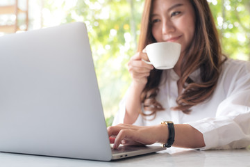 Closeup image of a beautiful Asian woman using laptop while drinking coffee in cafe