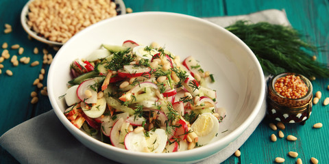 Salad with vegetables and eggs on the colorful blue background. Close up. European cuisine. Radish, cucumber, quail eggs and pine nuts. Ovo vegetarian dish. Wide photo.